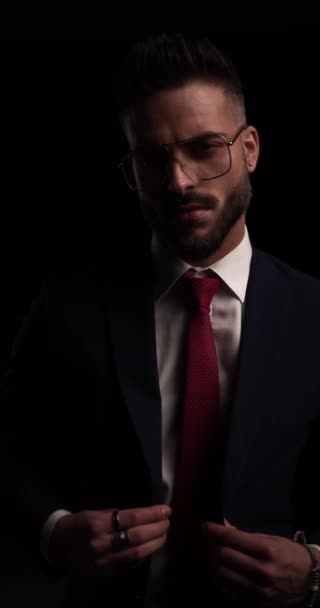 jeune homme confiant portant des lunettes, regardant de côté, fermant la combinaison et croisant les bras dans l'obscurité - Séquence, vidéo