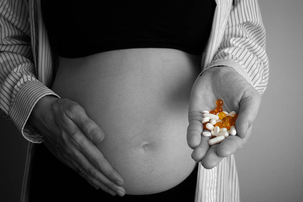 Pregnant woman holding pills on her hand. The concept of taking antidepressants and drugs during pregnancy. Black and white photo. - Foto, Imagem