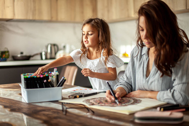 Young beautiful mother and cute daughter draw a mandala pattern together. Artistic markers and colored pencils. - Foto, Imagem