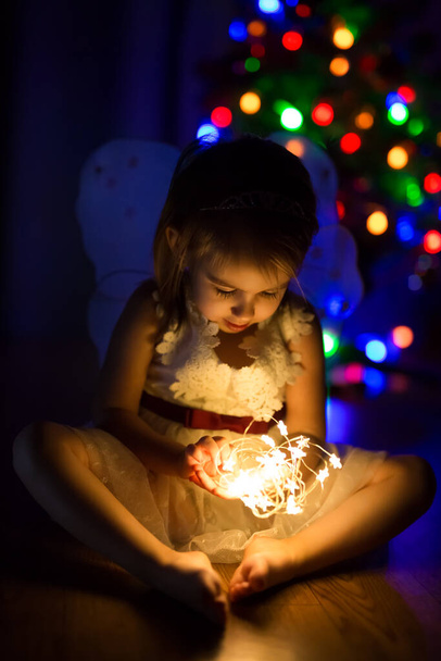 Ein Mädchen hält in der Nacht auf Heiligabend sternförmige Lichter in ihren Händen und wartet auf Wunder. Bunte Lichter des Weihnachtsbaums bokeh auf einem dunklen Hintergrund. Magische Momente im neuen Jahr - Foto, Bild
