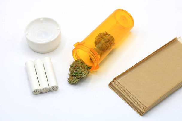Marihuana knoppen in een oranje pot vergezeld van rookpapier en geïsoleerde filters op een witte achtergrond - Foto, afbeelding