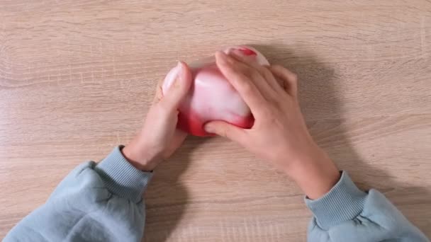 Playing with slime, stretching the gooey substance for fun and stress relief. Close up and top view of female hand holding red and white shining slime and squeezing it. 4K video - Footage, Video
