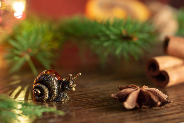 Σύνθεση Χριστουγέννων ή Πρωτοχρονιάς με ενθύμιο φιγούρας σαλιγκαριού δίπλα σε έλατο, ξυλάκια κανέλας και κάρδαμο. Επιλεκτική εστίαση - Φωτογραφία, εικόνα