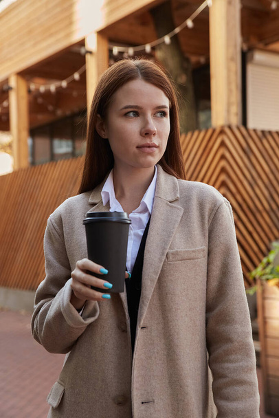 belle jeune femme caucasienne dans élégant manteau beige boire du café en plein air - Photo, image