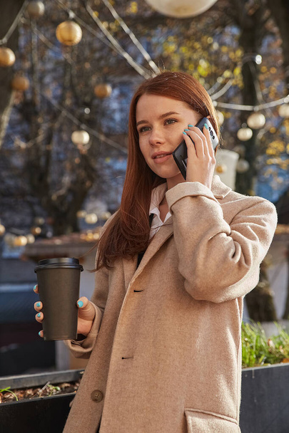 valkoihoinen nainen tyylikäs beige takki soittaa älypuhelimella, juo kahvia - Valokuva, kuva