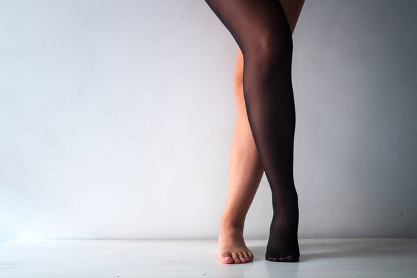Brunette nainen lyhyt ristissä jalat on pukeutunut vain musta sukka valkoisella taustalla - Valokuva, kuva