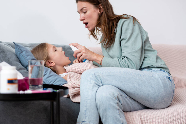 Girl has a sore throat and her mother sprays her medicine - Fotó, kép