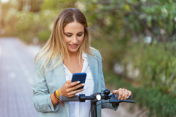 Femme utilisant un smartphone pour louer un scooter électrique - Photo, image
