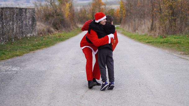 Meisje verkleed als kerstman knuffelt een kind - Foto, afbeelding