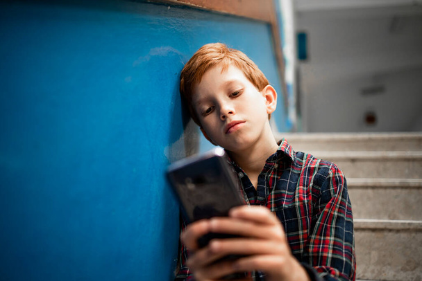 Young caucasian boy playing video games on his smart phone before class in school. - 写真・画像