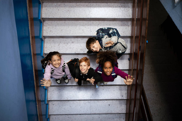 Blick von oben auf Kinder, die auf dem Schulflur in die Kamera winken und ins Klassenzimmer gehen. - Foto, Bild