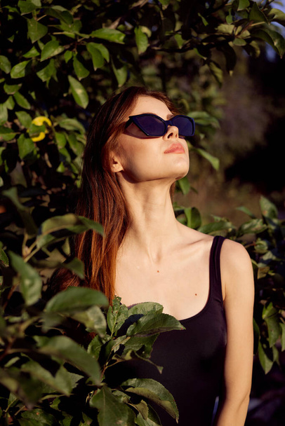 pretty woman in sunglasses in summer outdoors green leaves - Fotó, kép