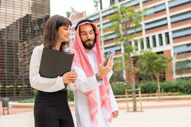 Dois parceiros de negócios diversificados árabe homem e mulher branca usando smartphone durante reunião na cidade - Foto, Imagem
