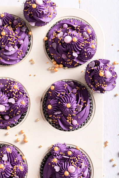 Homemade cupcakes made of purple cream for fat thursday. Purple dessert with golden sprinkles in baking tray. - Valokuva, kuva