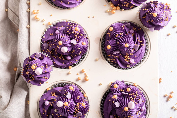 Unique cupcakes with flower shaped purple cream. Purple dessert with golden sprinkles in baking tray. - Foto, immagini