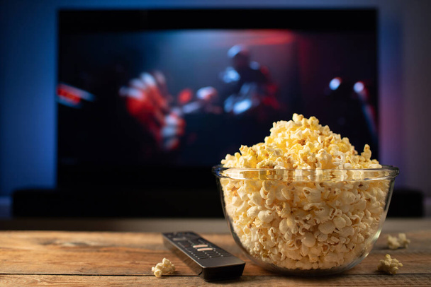 Skleněná mísa popcornu a dálkové ovládání na pozadí televizoru funguje. Večer příjemné sledování filmu nebo televizní seriál doma. - Fotografie, Obrázek