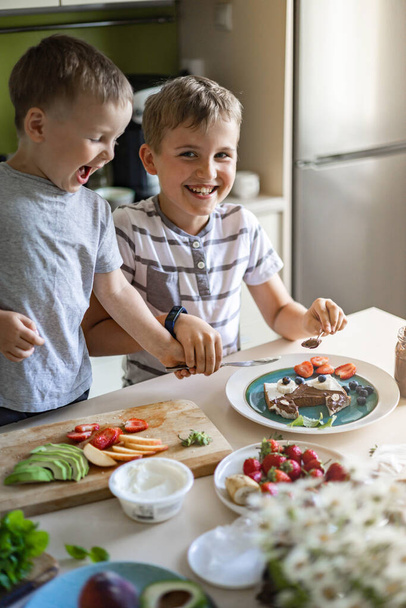 Two male little friends brother decorating morning sandwich with fruit, berries and chocolate paste - Foto, Bild