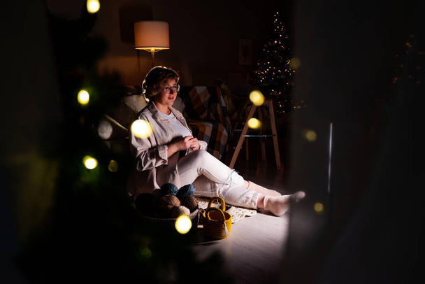 Kadın, Noel akşamı rahat bir evde iplik anahtarıyla sepet örüyor. Aile Noel gelenekleri. - Fotoğraf, Görsel