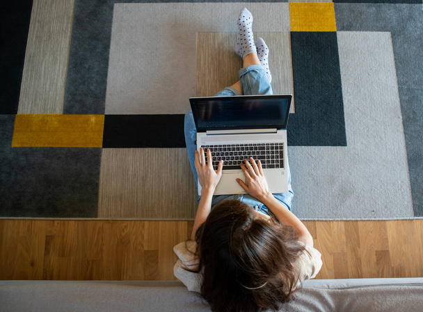 Vista de cima de mulher trabalhando em um laptop enquanto sentado no chão. Uma jovem está programando - Foto, Imagem