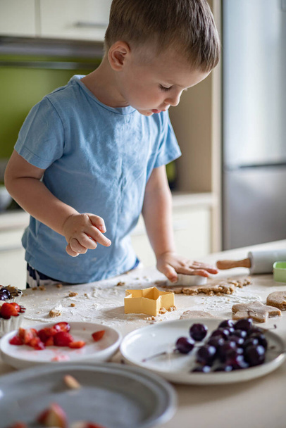Cheerful male baby cooking homemade summer dessert with fruits and berries at home kitchen - Foto, immagini