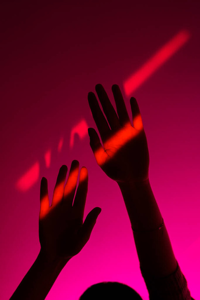 Žena ruku gestikuluje s otevřenou rukou přes módní růžové pozadí, neonově červené skvrny na zápěstí. Minimalismus. - Fotografie, Obrázek