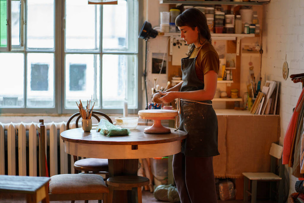 Giovane creatore di vasellame femminile lavorare con argilla sulla ruota ceramica nello spazio creativo o studio professionale - Foto, immagini