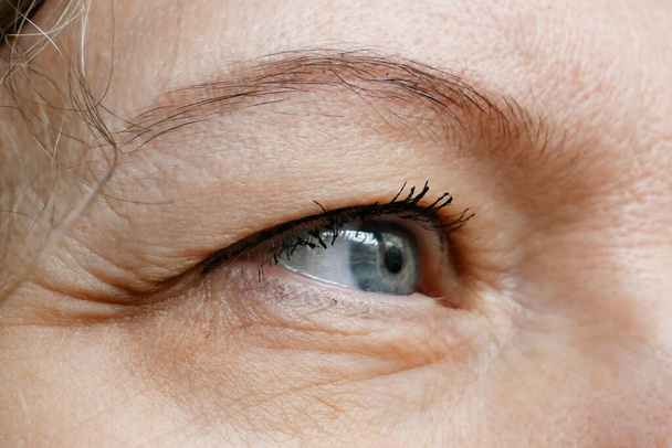 vrouw van middelbare leeftijd doet corrigerende oogmake-up om het hangende ooglid te corrigeren. Ptosis is een hangende van het bovenste ooglid, lui oog. Cosmetologie en gezichtsconcept, close-up - Foto, afbeelding