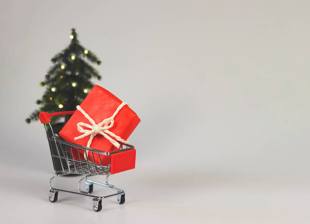 Vista frontal de la caja de regalo roja en el carrito de la compra, con el árbol de Navidad onf fondo blanco con espacio de copia... - Foto, imagen