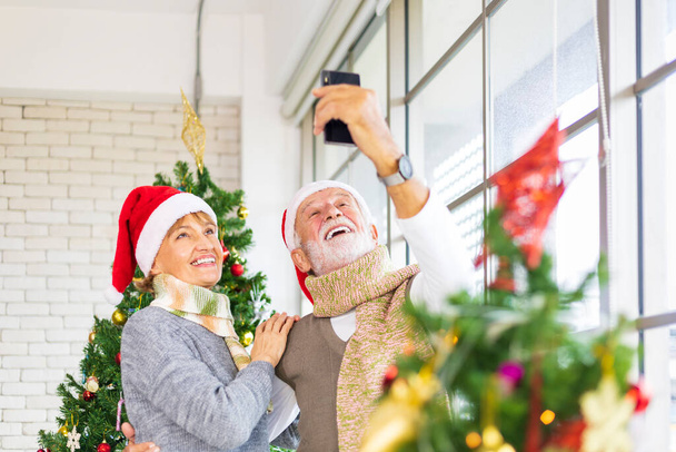 Старшая кавказская пара празднует Рождество вместе в счастье и волнение дома с Сантой шляпой и рождественской елкой - Фото, изображение