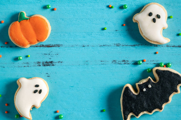 Top view of Halloween festive decorated baked icing gingerbread sugar cookies on blue background with copy space and flat lay. - Foto, imagen