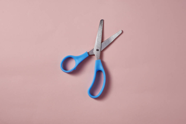 A top view of the blue scissors on the pink surface - Foto, Bild
