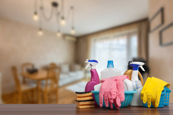 Концепция услуг по уборке дома с расходными материалами. Close up of cleaning supplies in front of living room
. - Фото, изображение