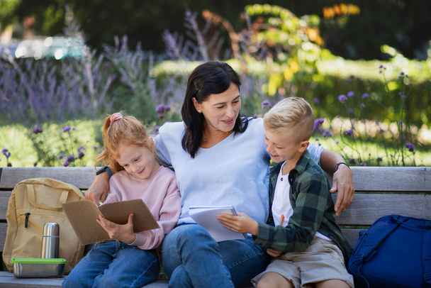 Happy senior woman with grandchildren sitting on bench and helping with homework outdoors in park. - Foto, Bild
