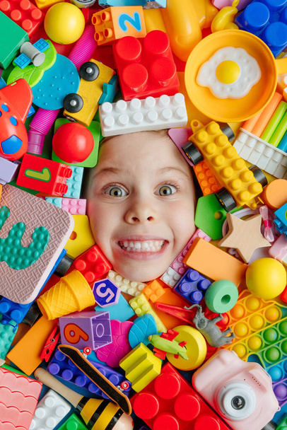 Pieni tyttö makaa taustalla eri värikkäitä muovisia ja puisia leluja. Lapsuuden käsite. Top view, tasainen lay. - Valokuva, kuva