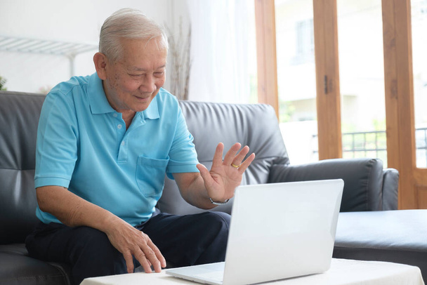 Starszy mężczyzna wykonujący połączenie wideo i machający na ekranie, rozmawiający z dziećmi, porozumiewający się z przyjacielem na odległość, starsza generacja nowoczesnych technologii łatwa koncepcja wygodnego użytkowania - Zdjęcie, obraz