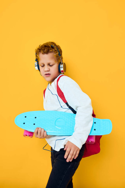 menino alegre com skate em fones de ouvido fundo amarelo - Foto, Imagem