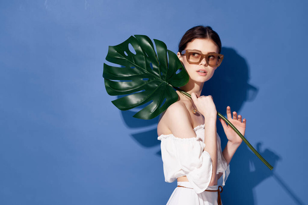 Güzel bir kadın elinde palmiye yaprağı tutarken egzotik moda mavisi arka plan - Fotoğraf, Görsel