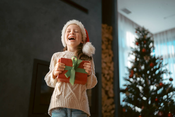 Merry Christmas and Happy Holidays! Cheerful cute child girl with gift. Kid is having fun near tree. - Zdjęcie, obraz