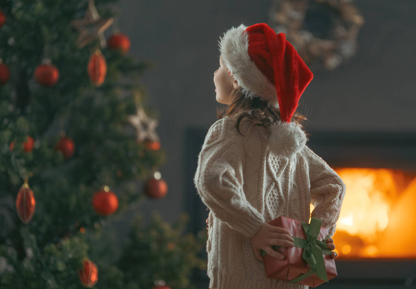 Merry Christmas and Happy Holidays! Cheerful cute child girl with gift. Kid is having fun near tree. - Φωτογραφία, εικόνα