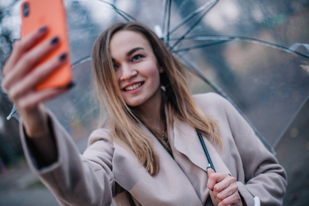 Happy young girl with a transparent umbrella takes a selfie on a rainy day - Photo, image