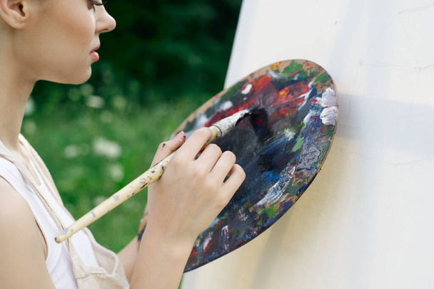 woman artist paints palette easel nature drawing - Фото, изображение