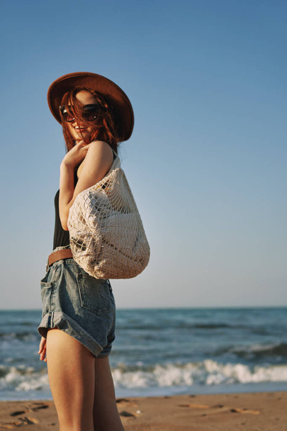 cheerful woman in a hat with sunglasses walking with a bag - Photo, image