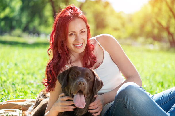 Young attractive woman hugs her dog in the park. - Photo, image