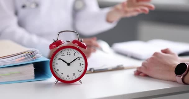 Reloj despertador rojo de pie en la mesa cerca del médico y el paciente primer plano 4k película cámara lenta - Imágenes, Vídeo