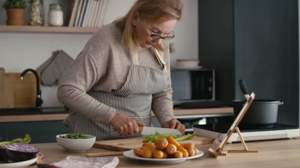 Valkoihoinen vanhempi nainen kuorinta porkkana kun ruoanlaitto keittiössä. Laukaus punaisella heliumkameralla 8K    - Materiaali, video