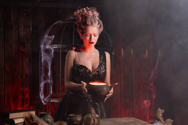 Halloween witch with cauldron. Beautiful young woman conjuring, making witchcraft. Standing spooky dungeon dark room. Enchantress prepare love potion use magic spell - Photo, Image
