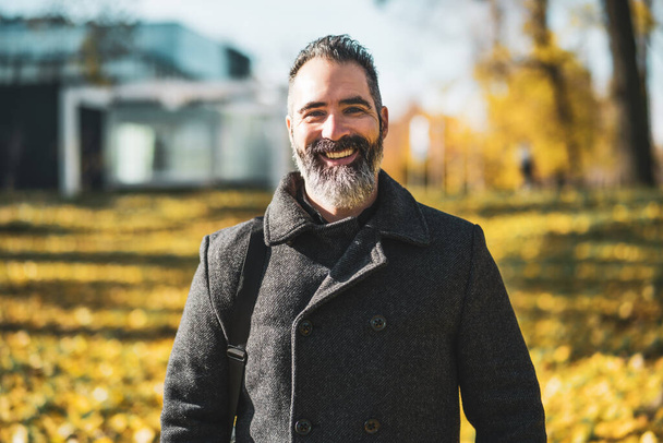 Портрет щасливого бізнесмена в парку восени. Чорний бородатий чоловік посміхається
. - Фото, зображення