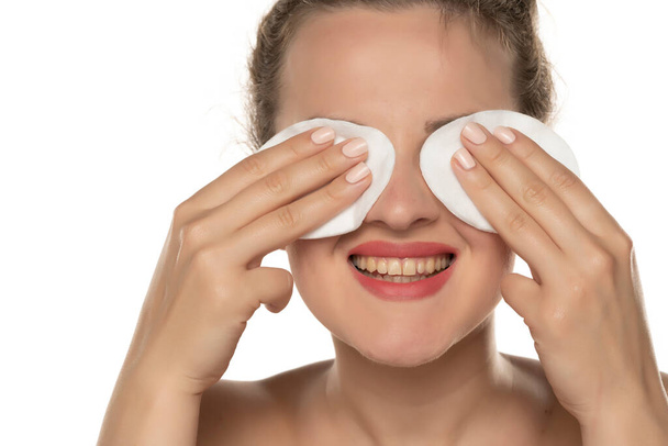 Joven mujer rubia feliz usando almohadillas de algodón para quitar el maquillaje en el fondo blanco - Foto, imagen