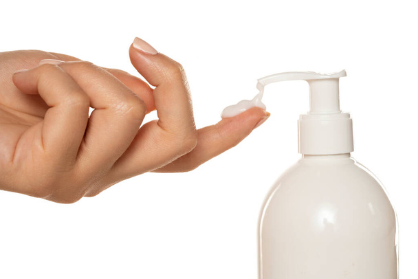 Pompalı bir şişe kozmetik ürünü beyaz arka planda bir kadının parmağına krem sürüyor. - Fotoğraf, Görsel