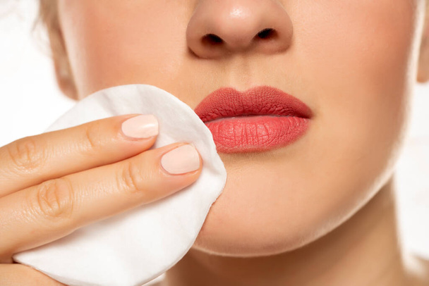 Clse up z sl kobieta czyści makijaż z jej ust z podkładką bawełnianą na białym tle - Zdjęcie, obraz